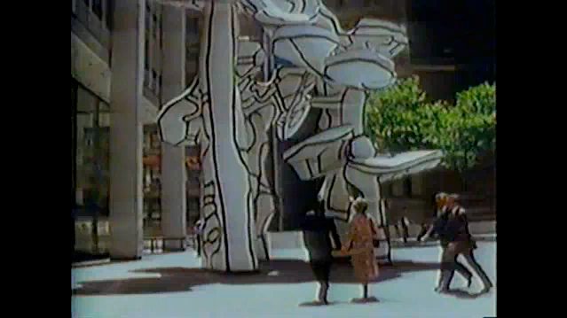 A still from _The Social Life of Small Urban Spaces_ by William H. Whyte. In a concrete public square stands an abstract sculpture. Some people stand by and stare at it, while some pass by.